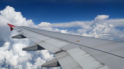 Wall Mural - 4K footage airplane flight. wing of an airplane flying above the white clouds and blue sky. beautiful aerial view from the window of the plane on travelling time by aircraft. holiday , vacation time