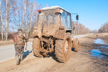 Wall Mural - Man stands back with tow near muddy wheeled tractor on roadside