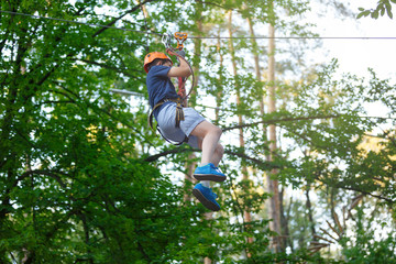 smiling little boy ziplining in treetop adventure park, healthy active lifestyle concept