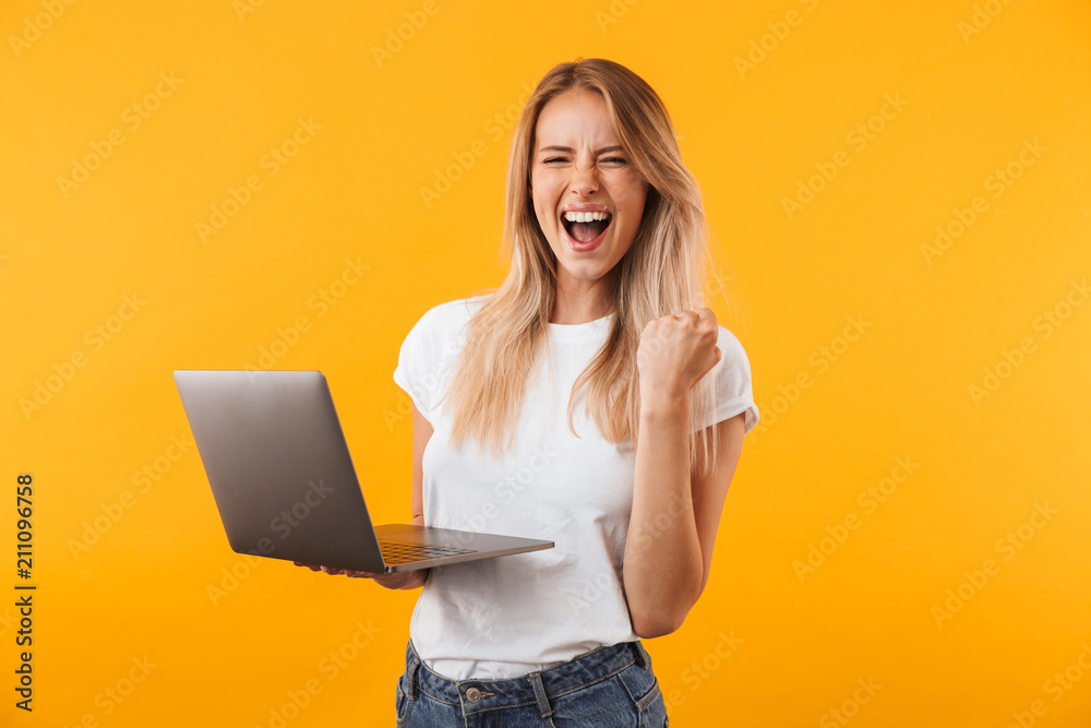 Portrait of an excited young blonde girl holding laptop - obrazy, fototapety, plakaty 