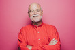 © Maskot - Portrait of smiling senior man with arms crossed against pink background