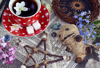 Voodoo doll with pentagram, cup of tea, mysterious objects and flowers. Occult, esoteric and divination still life. Halloween background with vintage objects and magic ritual