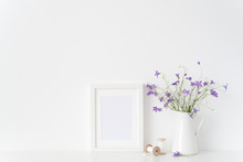 White Portrait Frame Mockup With Wild Flowers In Jar And Silk Ribbons Near White Wall. Empty Frame Mock Up For Presentation Design. Template Framing For Modern Art.
