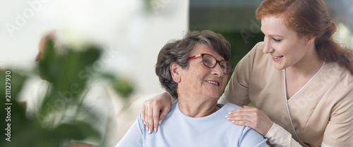 Fotomural Close-up of a tender caregiver with her hands on the shoulders of a senior woman inside her home