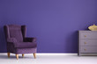 Retro armchair, chest of drawers with golden knobs and vase set on a violet, empty wall. Place your product