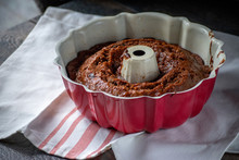 Red Bundt Pan With Baked Carrot Cake Inside Sitting On Red Striped Dish Towel On Farmhouse Table