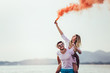 © Mediteraneo - Beautiful young couple with smoke bomb in hand is standing outdoors at golden summer background.