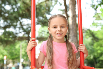 Wall Mural - Cute little girl playing on swings in park