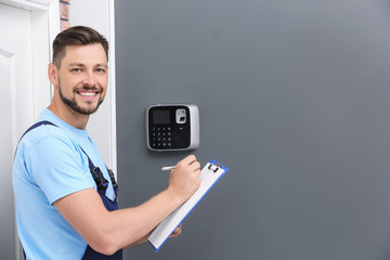 Wall Mural - Male technician with clipboard near installed alarm system indoors