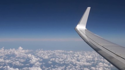 Wall Mural - 4K. Flying over the clouds in an airplane. Aircraft wing in flight trip with beautiful sky. Travel in plane. View of traveler in cabin-Adrian