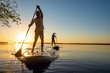 canvas print picture - Men, friends sail on a SUP boards in a rays of rising sun