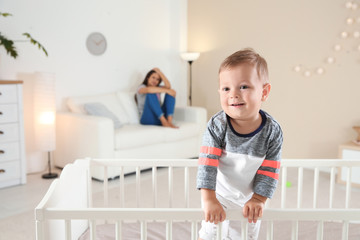 Wall Mural - Cute baby boy in crib and young mother suffering from postnatal depression on blurred background