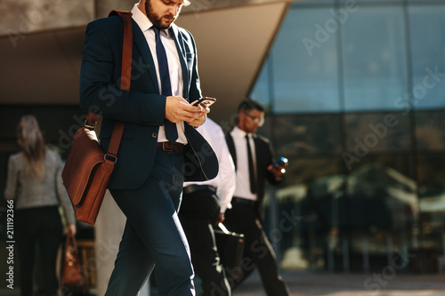 Plakat Business people using mobile phone while walking on street to of