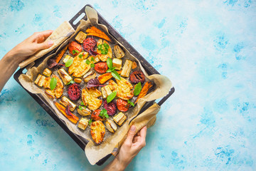 Baked vegetables on a baking sheet in the women's hands.