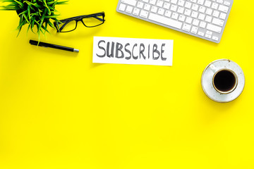 Poster - Email subscribe concept. Hand lettering subcribe on work desk with plant, glasses, computer keyboard, cup of coffee on yellow background top view copy space