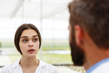 Wall Mural - Man and woman in laboratory robes talk to each other standing in the greenhouse