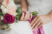 Beautiful Colorful Wedding Flowers In Hands Of Young Bride Sitting Alone In Home Interior. Fingernails With Beautiful Bridal Manicure And Engagement Ring. Horizontal Color Photography.