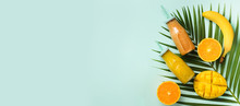 Exotic Orange, Banana, Pineapple, Mango Smoothie And Juicy Fruits On Palm Leaves Over Blue Background. Banner. Detox Summer Drink. Organic Fruits And Vegan Concept. Top View, Flat Lay, Copy Space