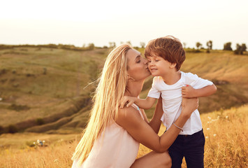 A mother kisses her son in nature in the summer.