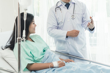 cheerful Asian doctor talking with young woman patient for monitoring and check up after surgery. doctor giving advice in the touchscreen to women to take care the lesion after out of hospital.