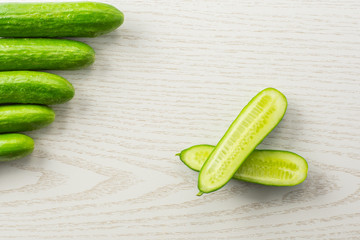 Wall Mural - Five fresh mini cucumbers and one cut in two halves flatlay on grey wood background.