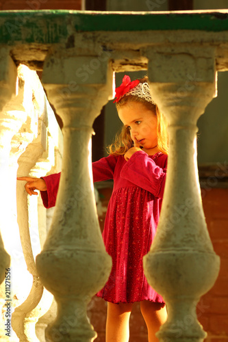 Fotografie, Obraz Sunlit portrait of a cute toddler girl behind old balcony banisters