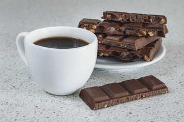 White cup with black coffee and chocolate on a white stone table