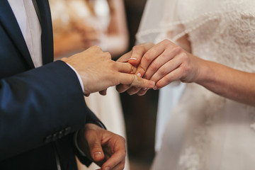 beautiful bride and groom hands exchanging wedding rings in church during wedding ceremony. spiritual holy matrimony. wedding couple and priest putting on rings