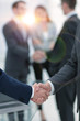© ASDF - Two businessmen shaking hands with colleagues  on background.