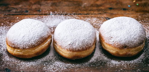 Wall Mural -  Krapfen with powder sugar, three and isolated on wooden background.