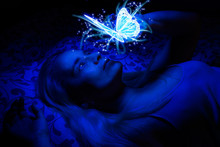 Concept Of A Woman Laying In Bed In The Dark, Illuminated With Blue Light From Floating Magical Butterfly Above Her, Her Hand Lightly Touching It