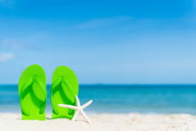 Green Flip Flop With Starfish On Sandy Beach, Green Sea And Blue Sky Background For Summer Holiday And Vacation Concept.