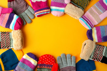 Mittens And Gloves On A Yellow Background. A Lot Of Mittens And Gloves Are Folded In A Frame On A Yellow Background. View From Above. Clothes For The Cold Seasons.