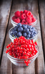 Wall Mural - Berries fresh arrangement in glass jars on white wooden table in studio. Red currant, raspberry, blueberry.