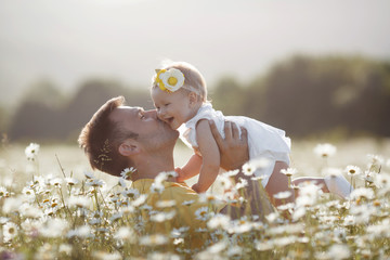 Happy young father having fun with newborn baby daughter in white chamomile field on warm summer day, family portrait together. Dad with baby girl outdoors, love. Bonding, family, new life