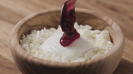 Wall Mural - Slow motion closeup adding cowberry jam to cottage cheese in wood bowl