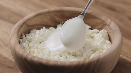 Wall Mural - Slow motion closeup adding sour cream to cottage cheese in wood bowl