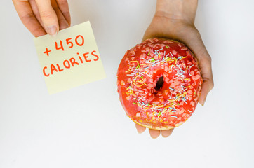 Woman hand holding pink donut with sprinkles extra calories fat fast food excess weight unhealthy on yellow background