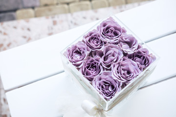 pastel purple hued roses in clear acrylic crystal flower box. square glass gift box. on white wooden