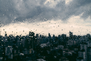 Rain over Bangkok: Out of focus cityscape behind the window glass with rain drops.