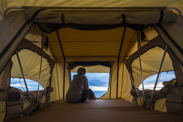 lonely independent strong middle age woman feeling the nature outdoor in a roof tent on the car. travel and lifestyle wanderlust concept for beautiful caucasian lady sitting in front of the ocean