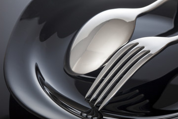 Wall Mural - Empty plate with spoon and fork on a black background