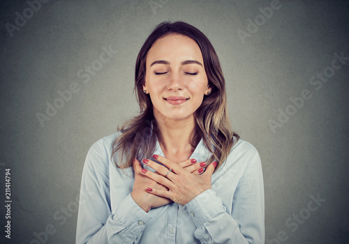 Faithful woman with eyes closed keeps hands on chest near heart, shows kindness Poster Mural XXL