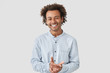 Waist up portrait of cheerful handsome African American male keeps hands together, smiles broadly, dressed in elegant shirt, being in high spirit after date with girlfriend, shares impressions