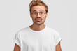 © WHstudio Leushin N - Funny curious male makes grimace, purses lips and looks doubtfully directly into camera, anticipates for something pleasant, has round eyes, wears big spectacles for good vision, poses indoor