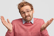 © wayhome.studio - Hesitant puzzled bearded male with clueless expression, can`t make choice between two items, wears glasses and pink sweater, poses against white background. Life perception and attitude concept