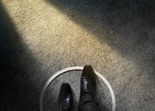 Comfort Zone Concept. Businessman With Formal Shoes Steps Over Circle Line To Outside The White Bound. Top View, Dark Tone, Light Shading On Cement Floor