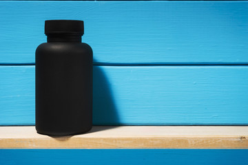 Black Bottle for pills on a wooden table. Beautiful blue background.