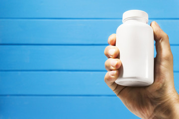 Poster - Hand hold white bottle for pills on a blue wooden background. 