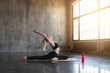 © deniskomarov - Flexible modern girl doing yoga practice in a loft studio, surrounded by bright sunlight.